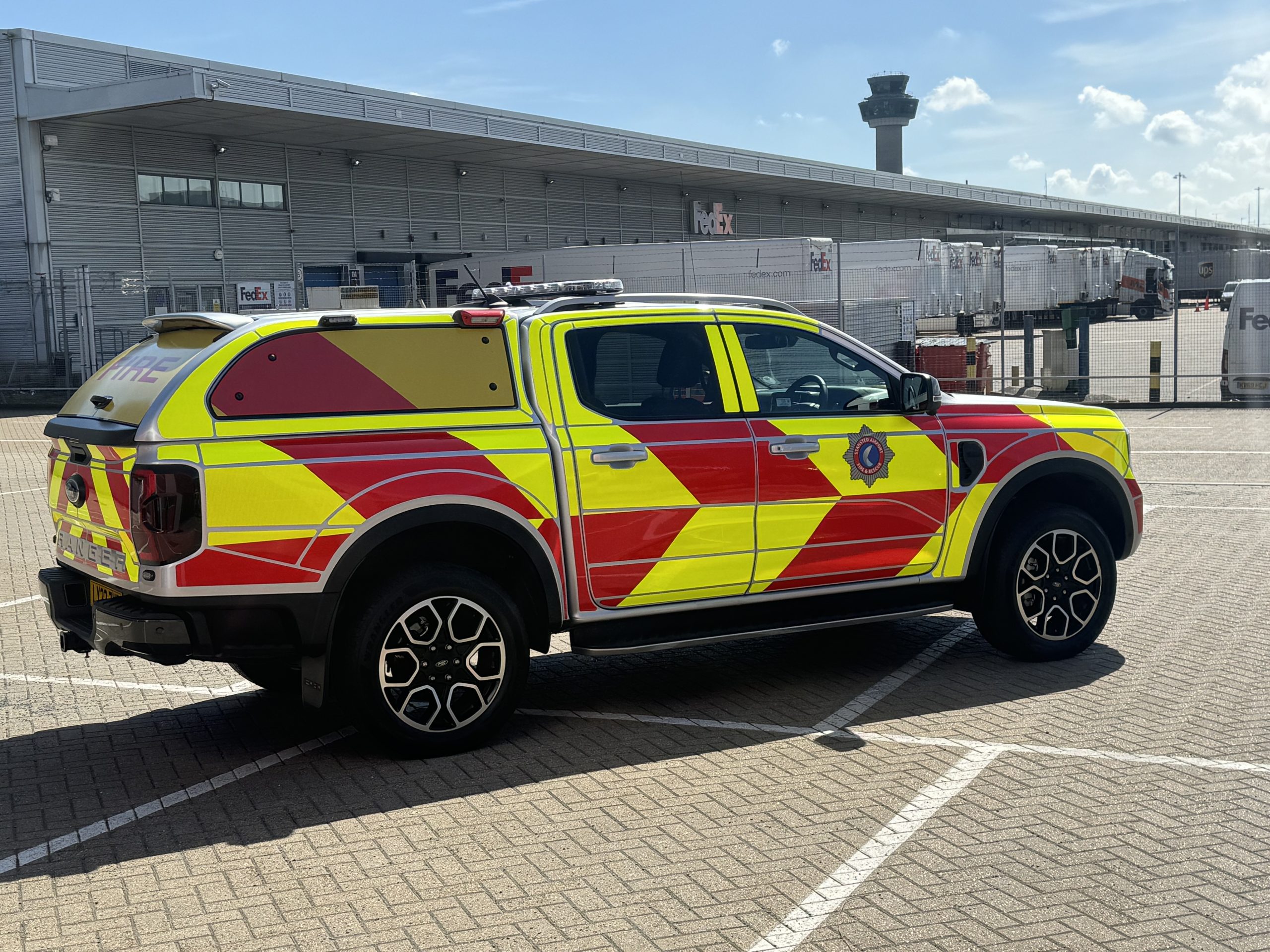 Stansted Airport is refreshing its fleet livery to deliver even more ‘stand-out’ support for operations both airside and in the local community. Andy Mott, Station Manager at Stansted Airport, has been working with Bluelite to design and install a new ‘herringbone’ livery for the fleet. The new markings have been debuted on a Ford Ranger, but now Andy aims to introduce the new design gradually across the entire fleet of 10 vehicles, which includes seven fire appliances. “For us, the livery is about ensuring the visibility of the fleet to ensure the safety of the team and other vehicles operating in the airport environment,” says Andy. “The new herringbone livery design helps us achieve this – and we also think it looks great and creates a really professional image for the service.” The airport’s operations fleet plays a unique emergency services role, being on stand-by for aircraft and airport incidents while at the same time providing firefighting support for the local community whenever needed. The Stansted fleet includes Rosenbauer and Scania fire appliances, a hose layer along with Ford Rangers, used for routine operations and driver training. “We’ve been working with Bluelite since 2010,” says Andy. “They’ve taken care of all our livery needs since then – they take a lot of time working with us to sure the best possible result. What they do is superb, from the design and installation to after service and replacement livery parts.”